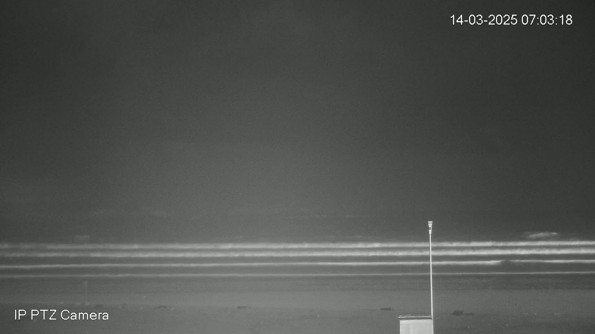 A dark, nighttime beach scene shows gently rolling waves under a cloudy sky, with a small, box-like object and a tall, thin pole near the bottom.
