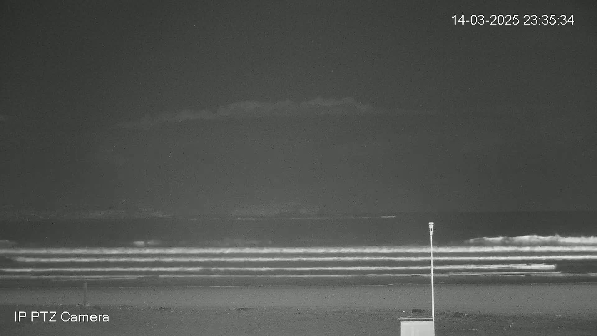 A nighttime beach scene shows a dark, cloudy sky over gently rolling waves and a sandy shore with a single lamppost.
