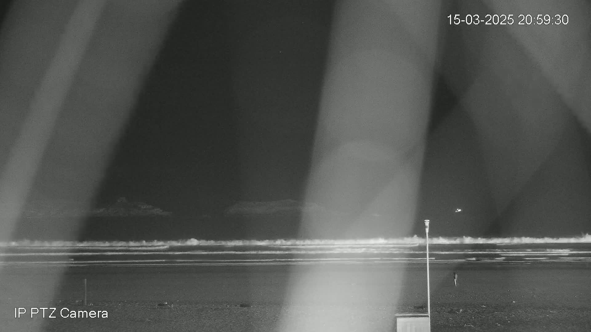 A nighttime beach scene shows waves gently rolling onto the shore under a dark sky, partially obscured by shadows from a foreground object.