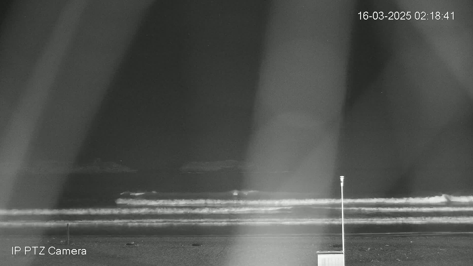 A nighttime beach scene with gentle waves rolling onto the shore under a dark sky.