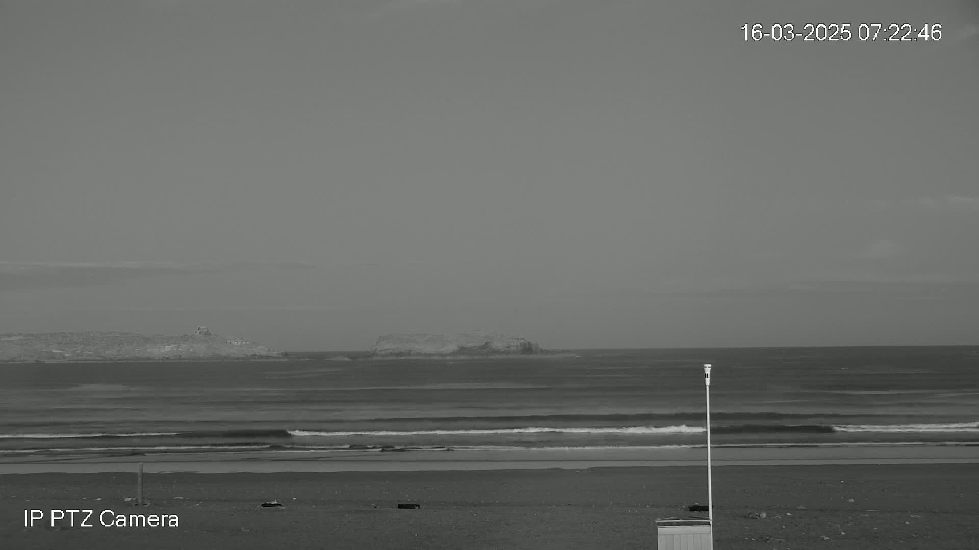 A grayscale image shows a beach with small waves under an overcast sky, and an island visible in the distance.