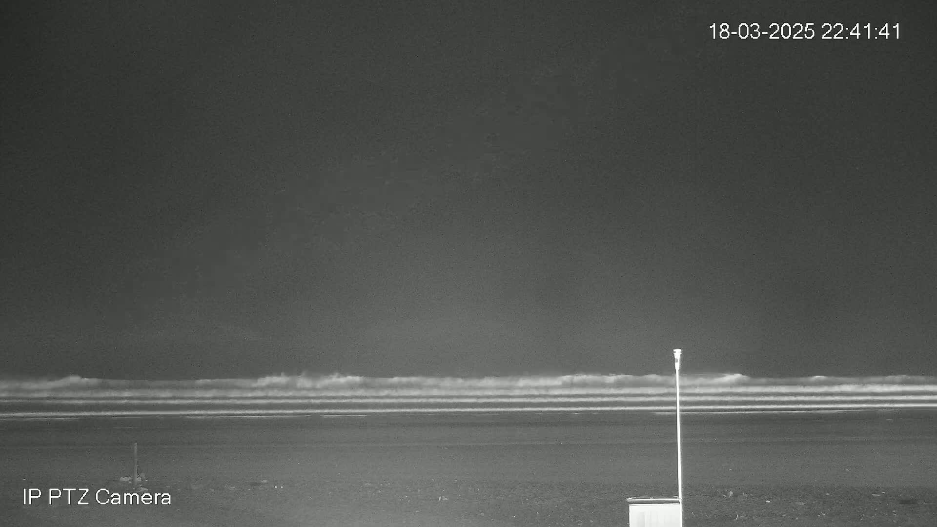 A dark nighttime beach scene shows moderate waves rolling onto the shore under a clear, dark sky.