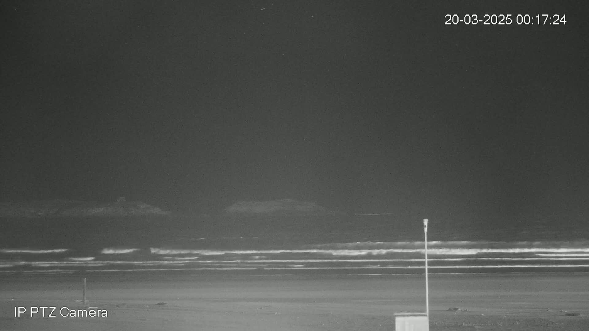 A dark, nighttime beach scene shows a relatively calm ocean with small waves under a clear sky.