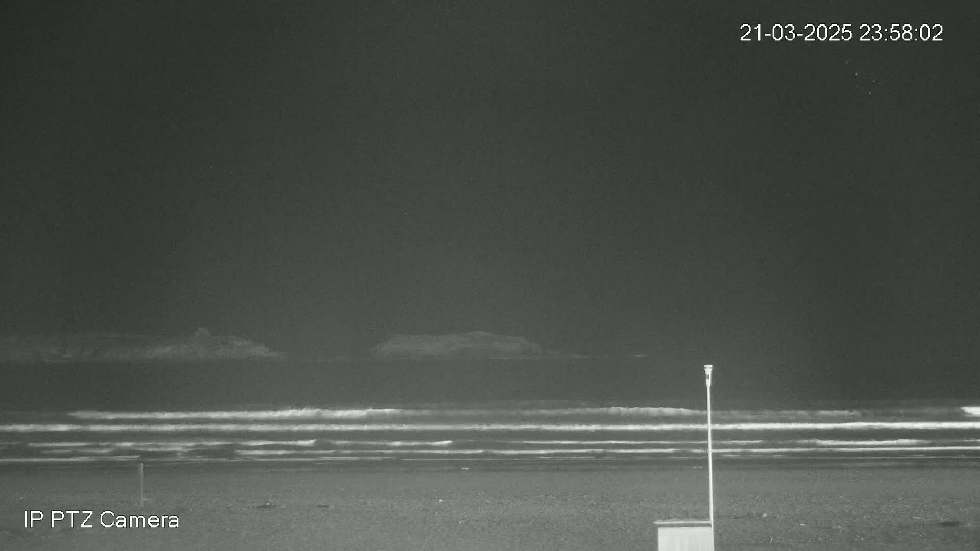 A dark, nighttime beach scene shows gentle waves lapping the shore under a clear sky.