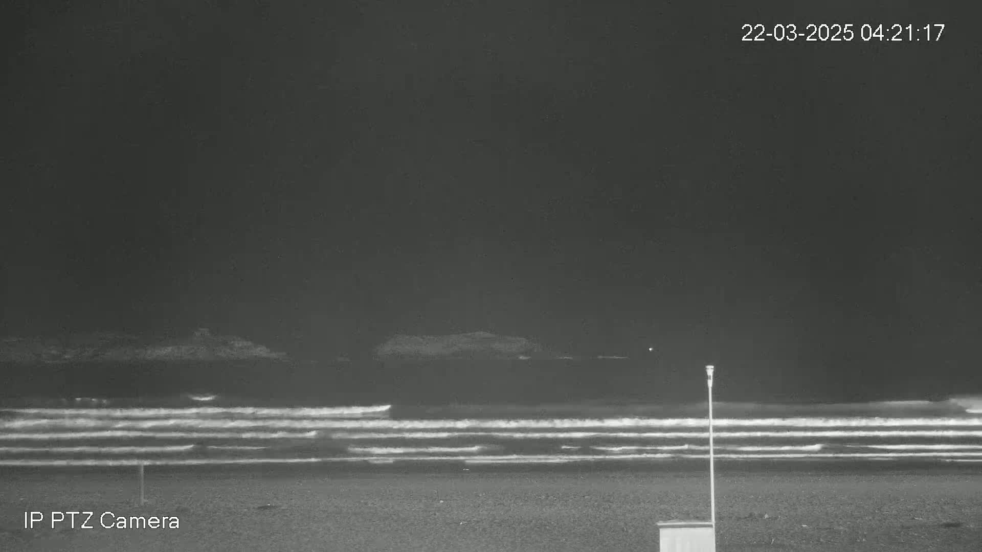A dark, nighttime beach scene shows gently rolling waves under a clear, black sky.