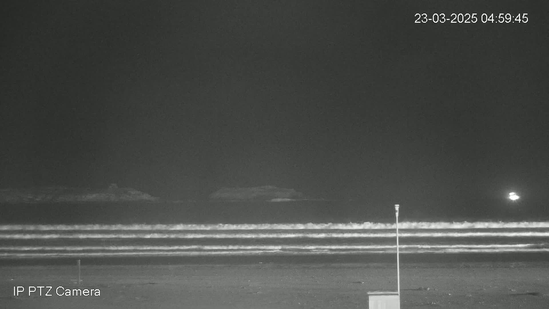 A dark beach at night shows gentle waves rolling onto the shore under a clear sky.