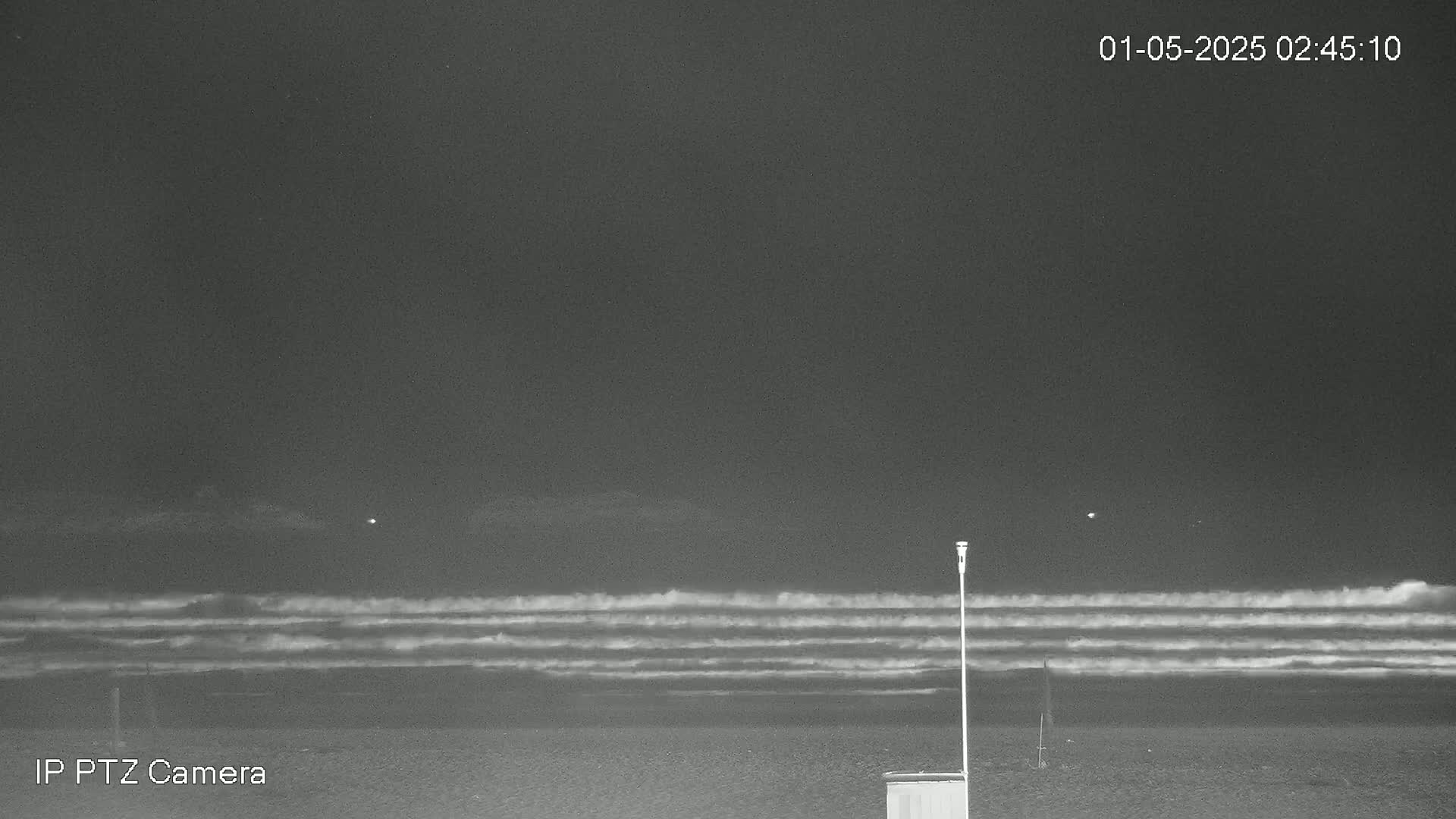 A nighttime beach scene shows dark, rolling waves under a mostly clear, dark sky.