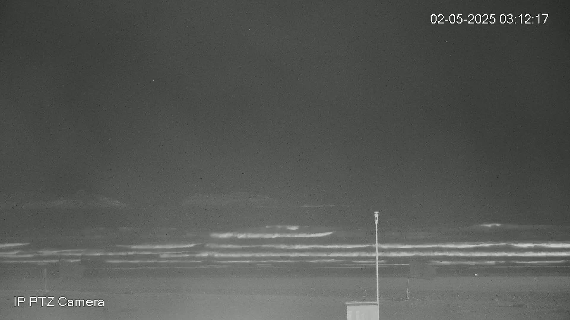 A dark, nighttime beach scene shows waves rolling onto the shore under a clear sky.