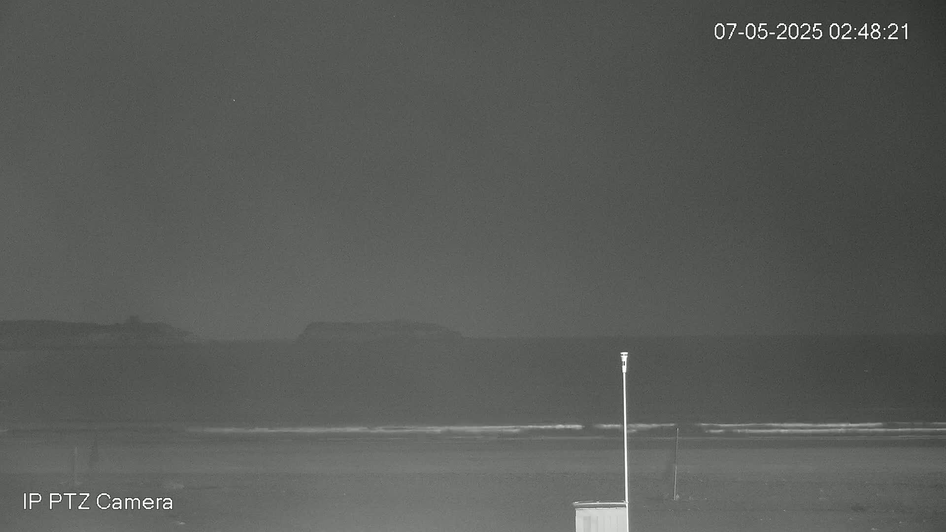 A nighttime beach scene shows a dark ocean with small waves lapping a sandy shore under a clear, dark sky.