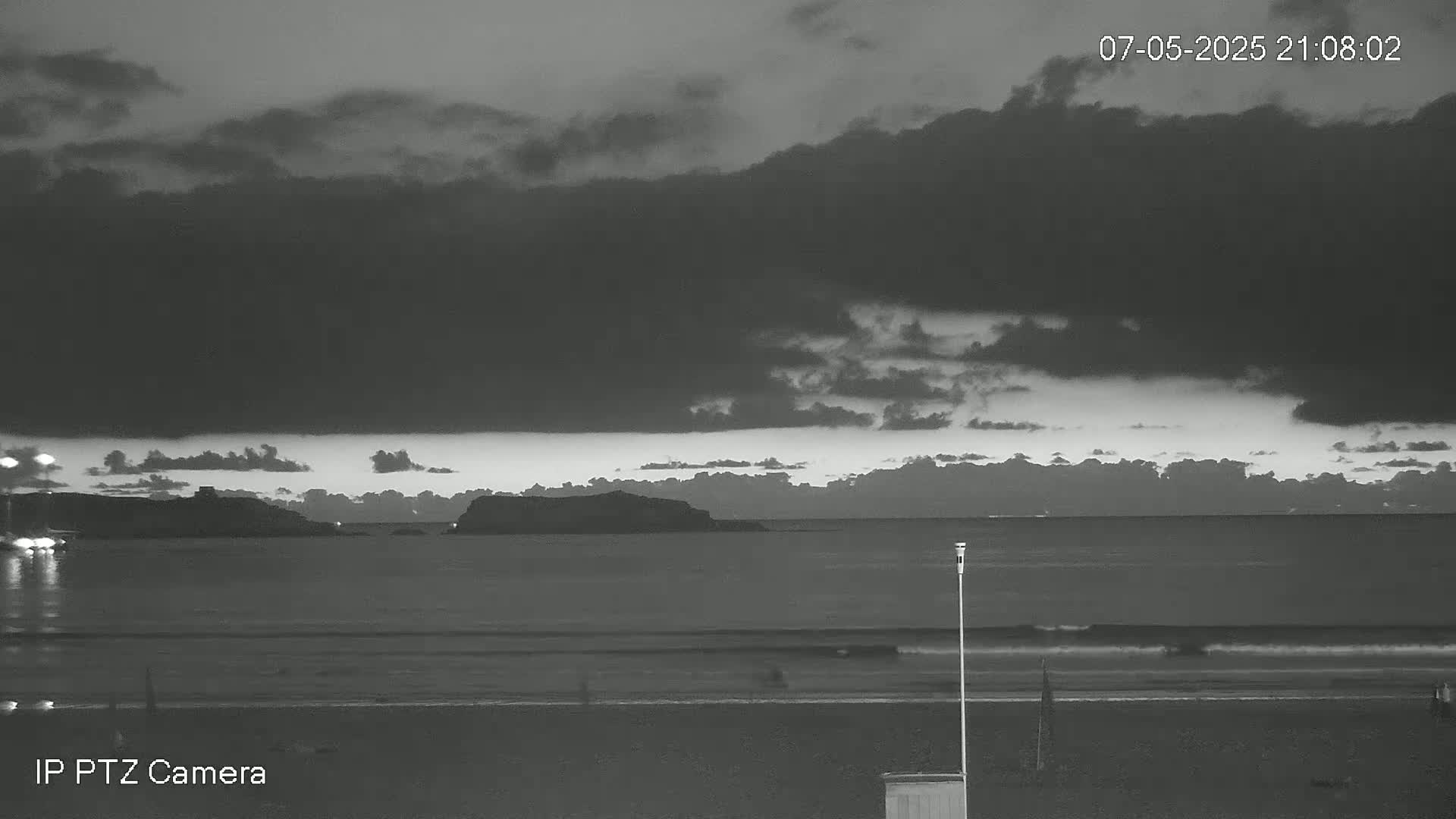 A dark, cloudy night scene shows a calm ocean with a small island in the distance and a sandy beach in the foreground.