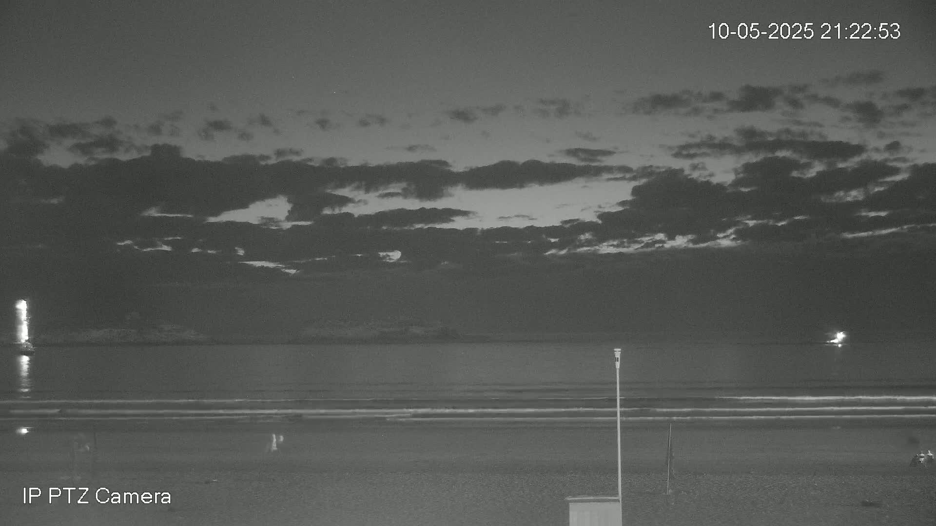 A nighttime beach scene under a partly cloudy sky shows a calm ocean with a faint light on the horizon.