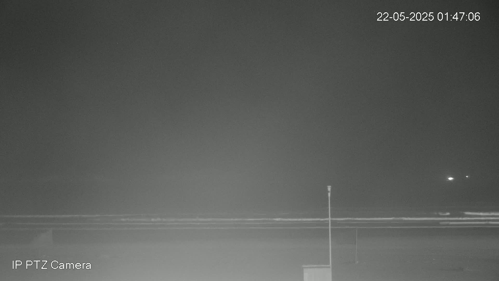 A nighttime, low-light image shows a dark beach with a calm ocean and a single pole standing near the shore.