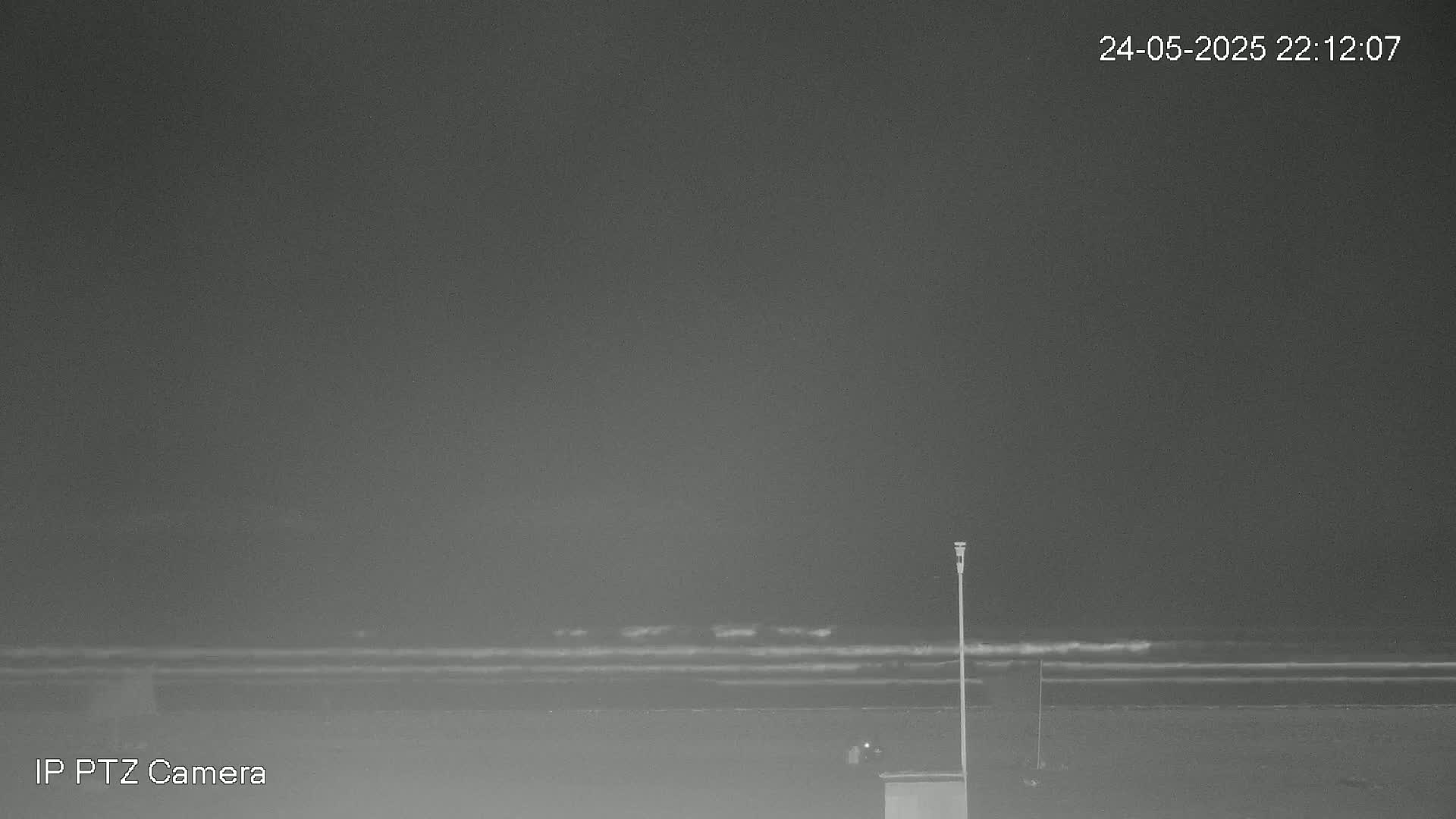 A nighttime beach scene shows calm waves lapping the shore under a dark, overcast sky.