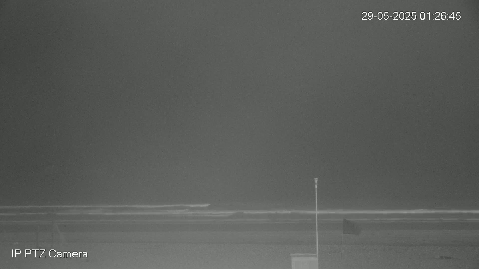 A nighttime, grayscale image shows a dark beach with a calm ocean under an overcast sky.