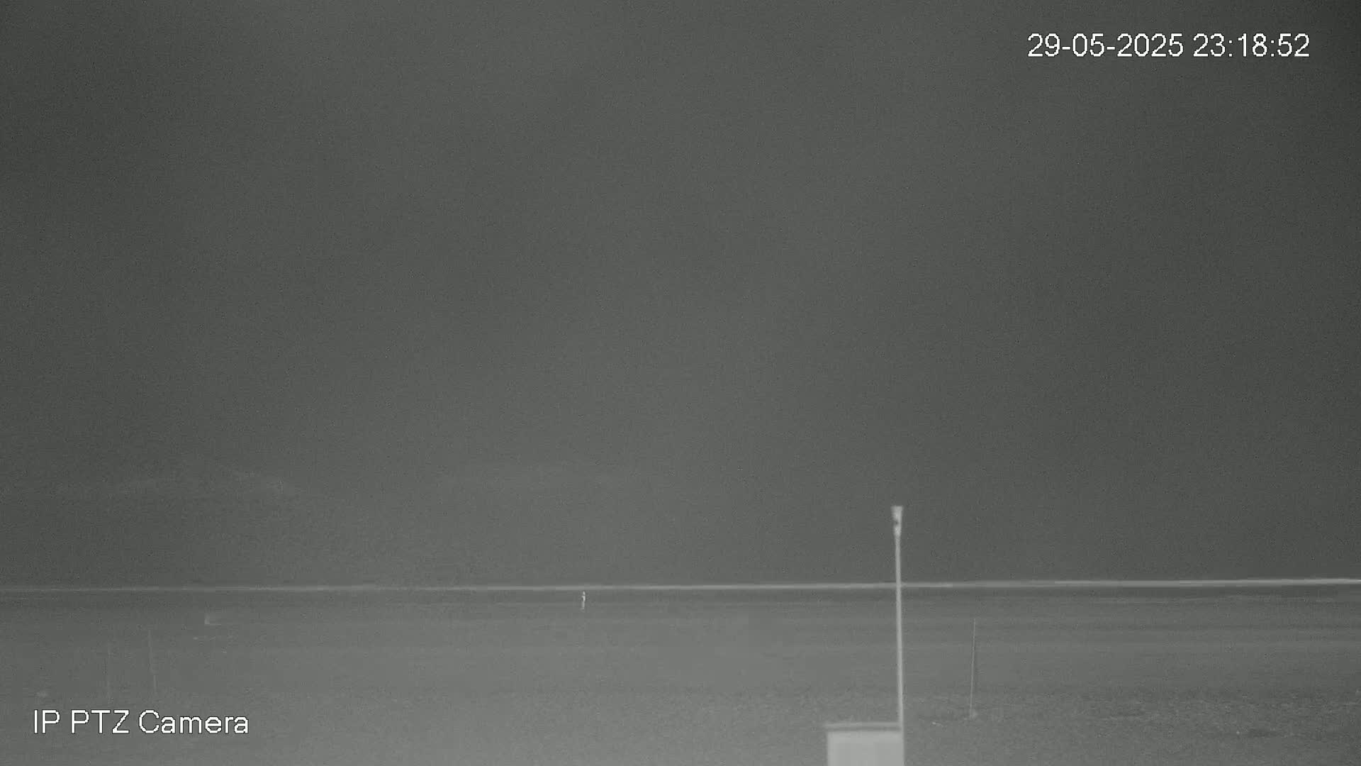 A nighttime low-light image shows a flat, dark landscape with a thin horizon line under a dark gray sky.