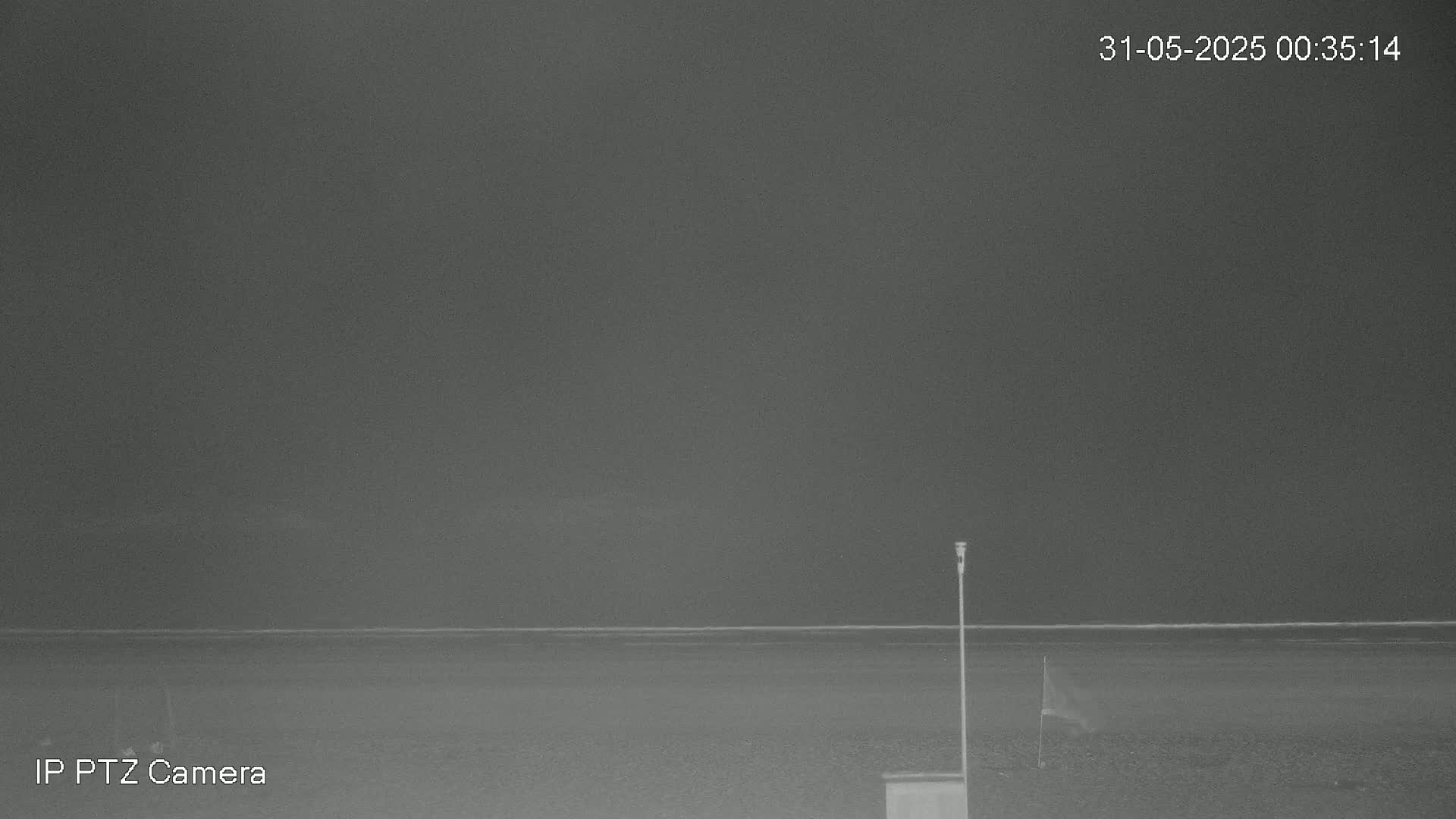 A nighttime, low-light image shows a flat, dark beach and a calm body of water under a dark, overcast sky.