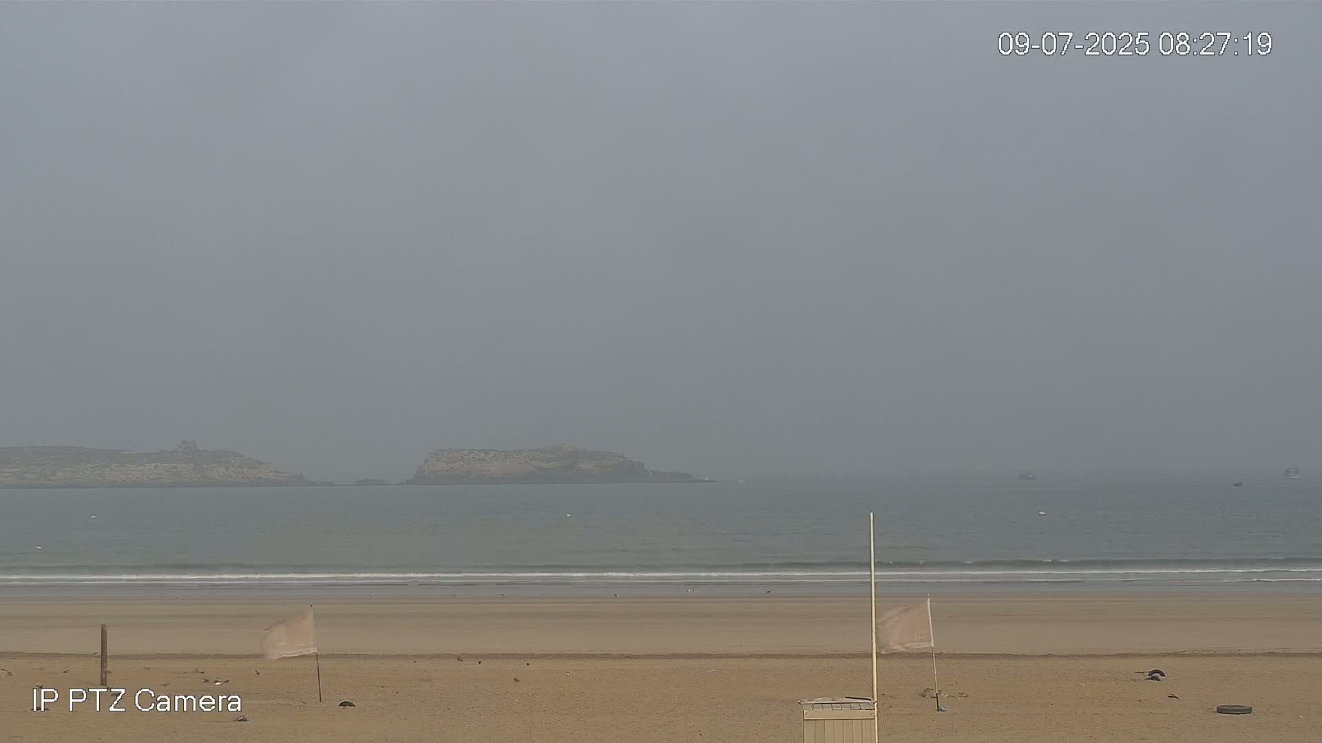 A hazy beach scene shows calm ocean waves lapping a sandy shore with small islands visible in the distance.