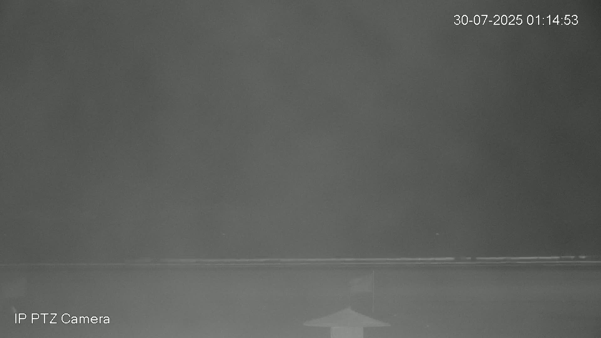 A nighttime, low-light view shows a dark, seemingly calm body of water under a hazy sky.