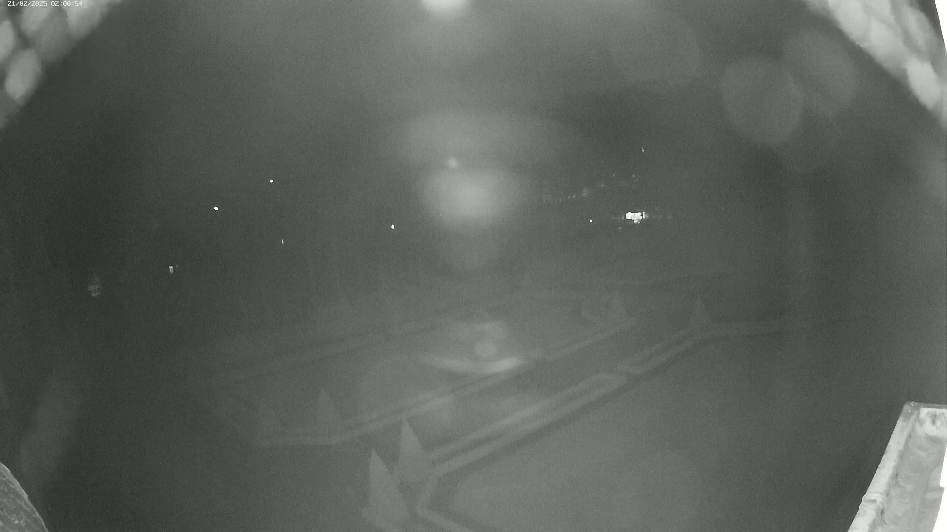 A nighttime, blurry view of a paved area, possibly a parking lot or roadway, with faint lights visible in the distance under hazy or foggy conditions.