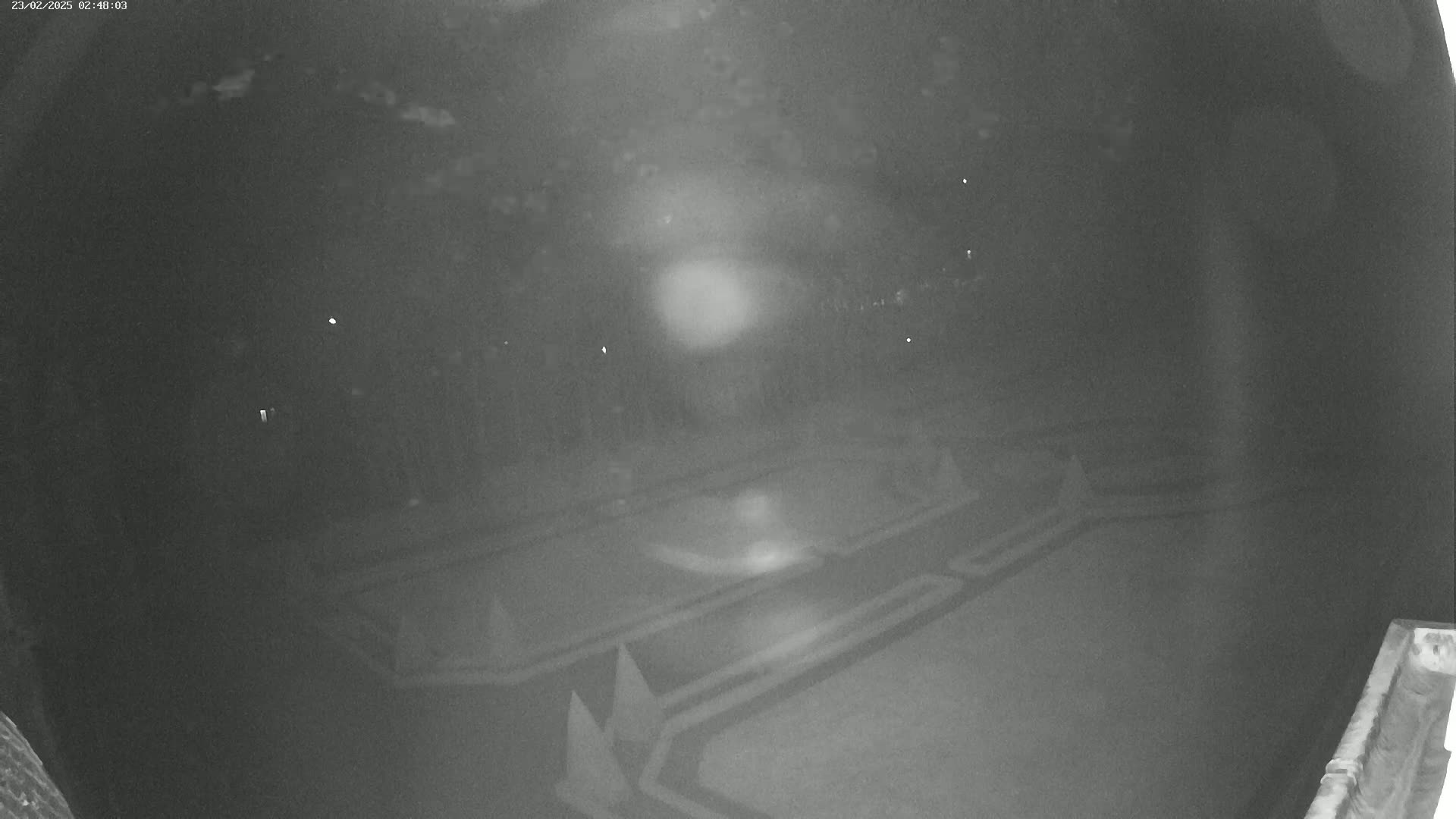 A nighttime, low-light view of an empty paved area with markings, possibly a parking lot or similar space.