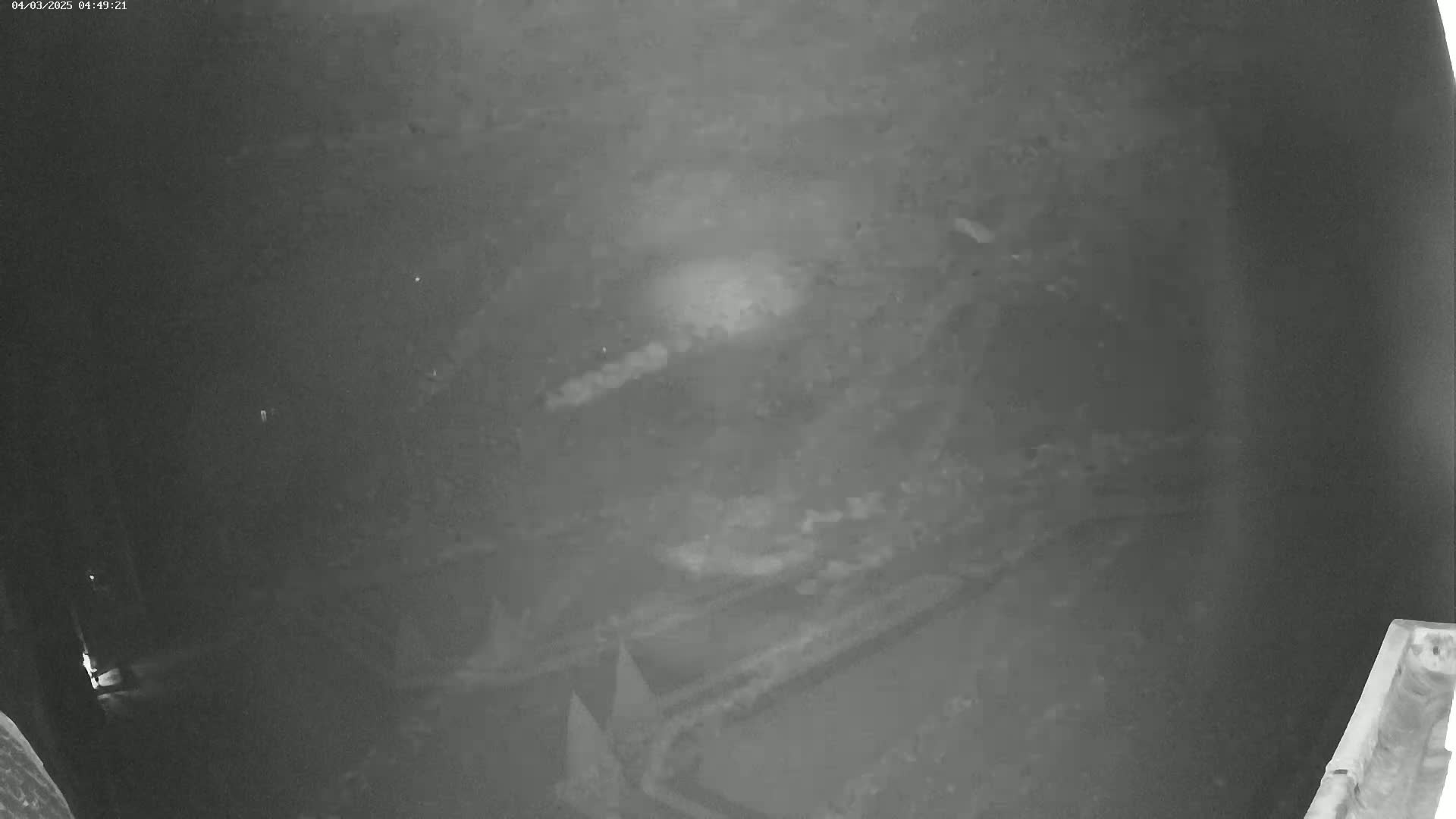 A low-light, grainy image shows a dark, possibly outdoor, scene at night with indistinct objects and a bright spot in the center.
