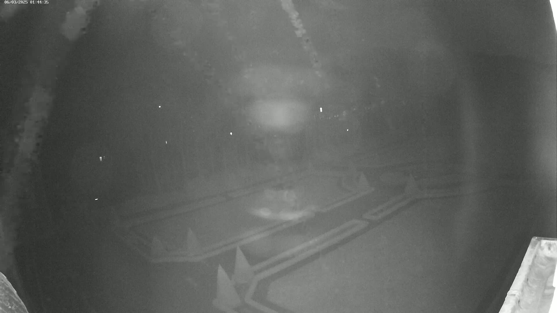 A nighttime low-light image shows a dark, possibly paved area with geometric patterns, possibly a park or parking lot, under a cloudy sky.