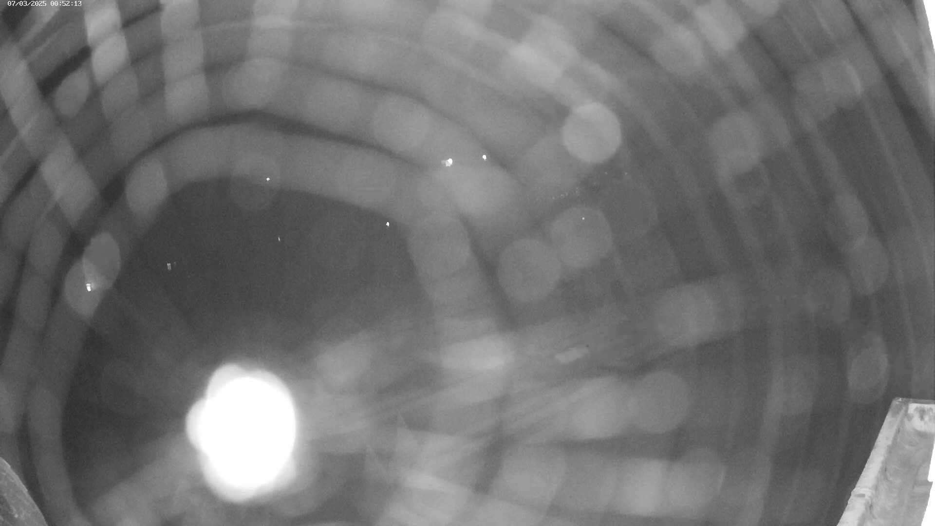 A blurry, grainy, black-and-white image shows a circular object, possibly a well or a large container, with indistinct shapes and bright spots of light.