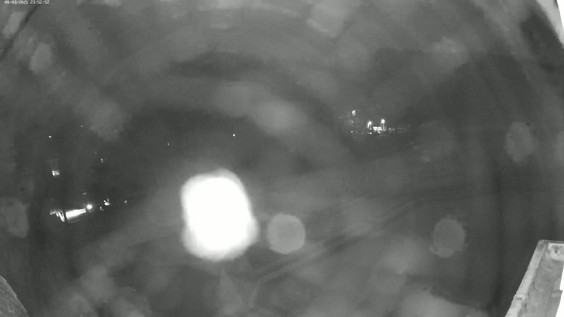 A nighttime, blurry security camera view shows a dark, possibly rainy, scene with faint lights and indistinct shapes in the distance.