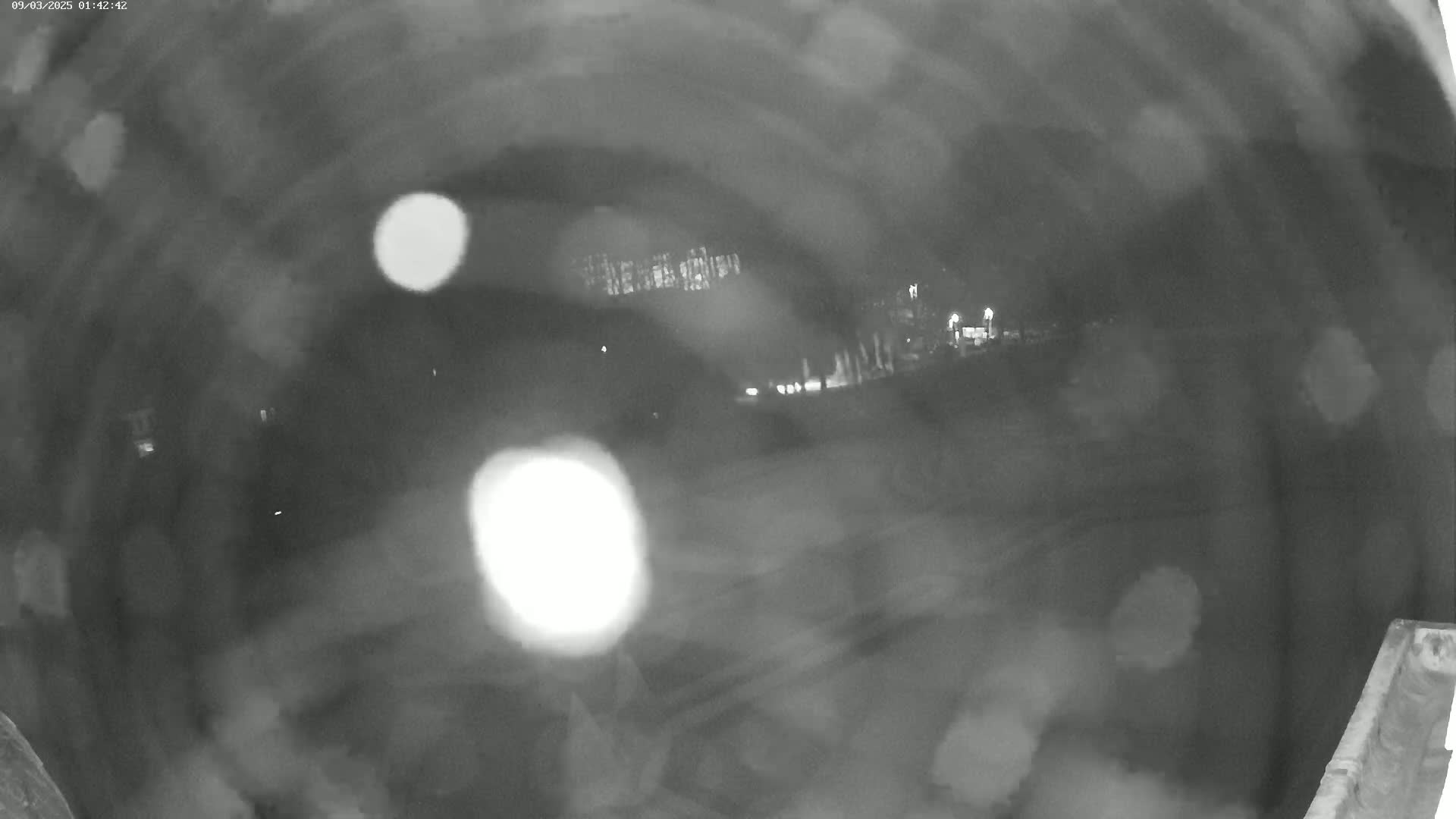 A blurry nighttime image from inside a tunnel shows indistinct lights and shapes in the distance through heavy rain or fog.