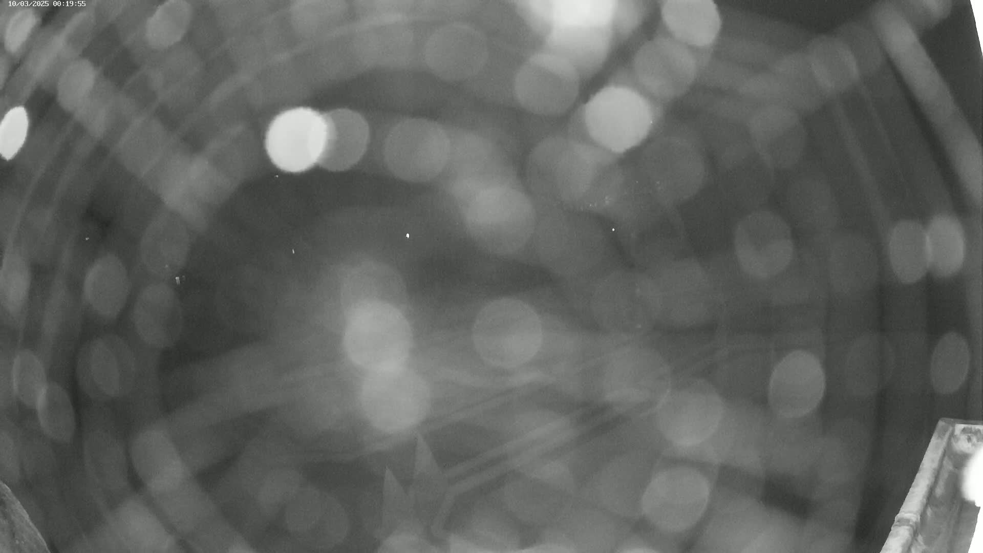 A blurry, nighttime image shows out-of-focus lights and indistinct shapes, possibly from rain or condensation on a lens.