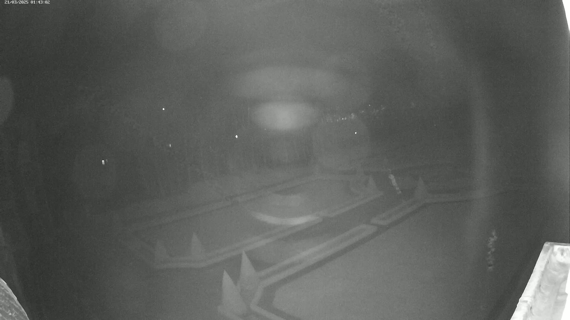 A nighttime, low-light image shows an overhead view of a dark, geometrically patterned outdoor area.
