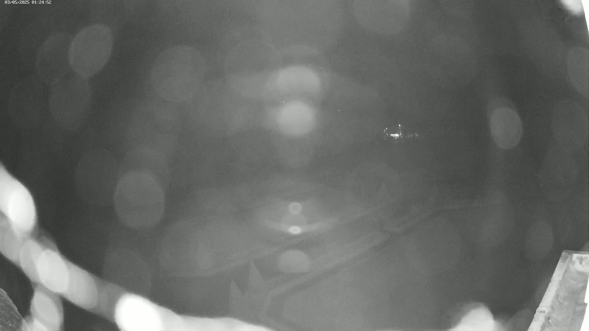 A blurry, nighttime, low-light image shows an indistinct view of a paved area, possibly a road or parking lot, with some out-of-focus lights in the distance.