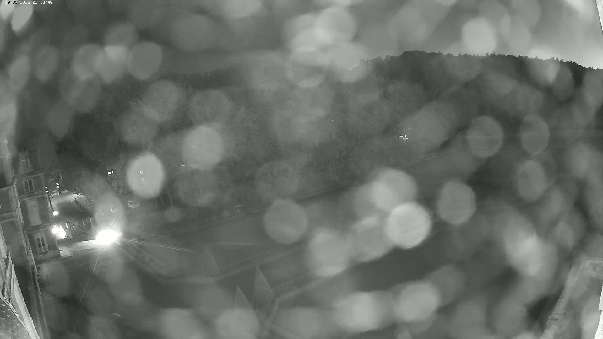 A nighttime, blurry view of a town or city, possibly from a high vantage point, with rain obscuring the view.