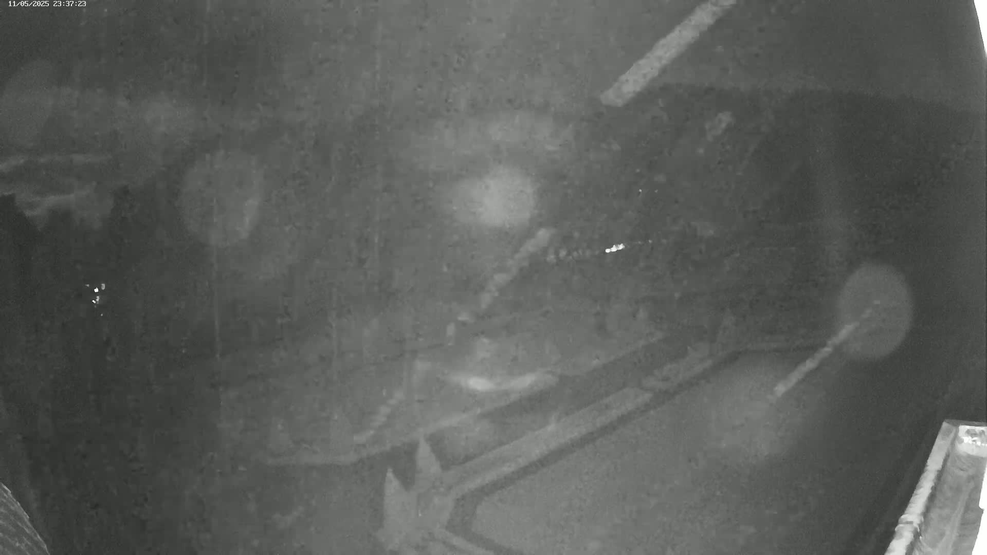 A grainy, nighttime security camera image shows a dark, paved area with faint light sources and indistinct shapes.