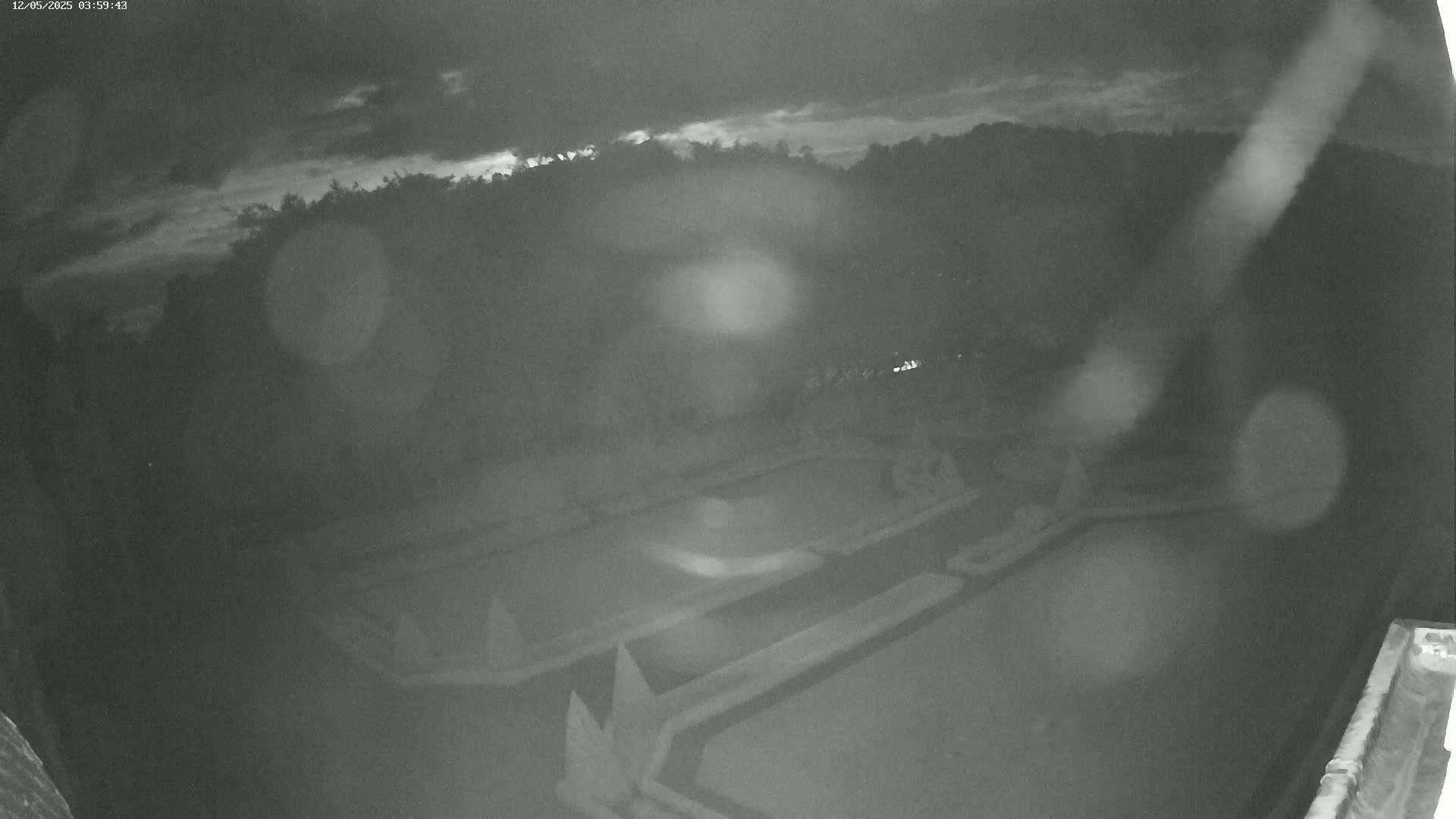 A nighttime, blurry, outdoor view of what appears to be an empty, geometrically patterned area, possibly a plaza or park, under a cloudy sky.