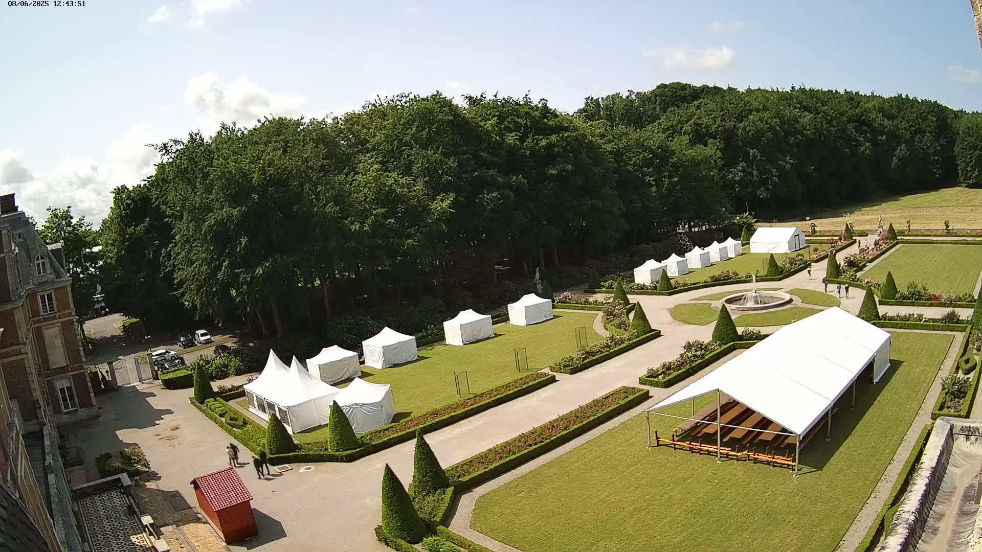 An aerial view of a formal garden with numerous white tents set up on a sunny day.