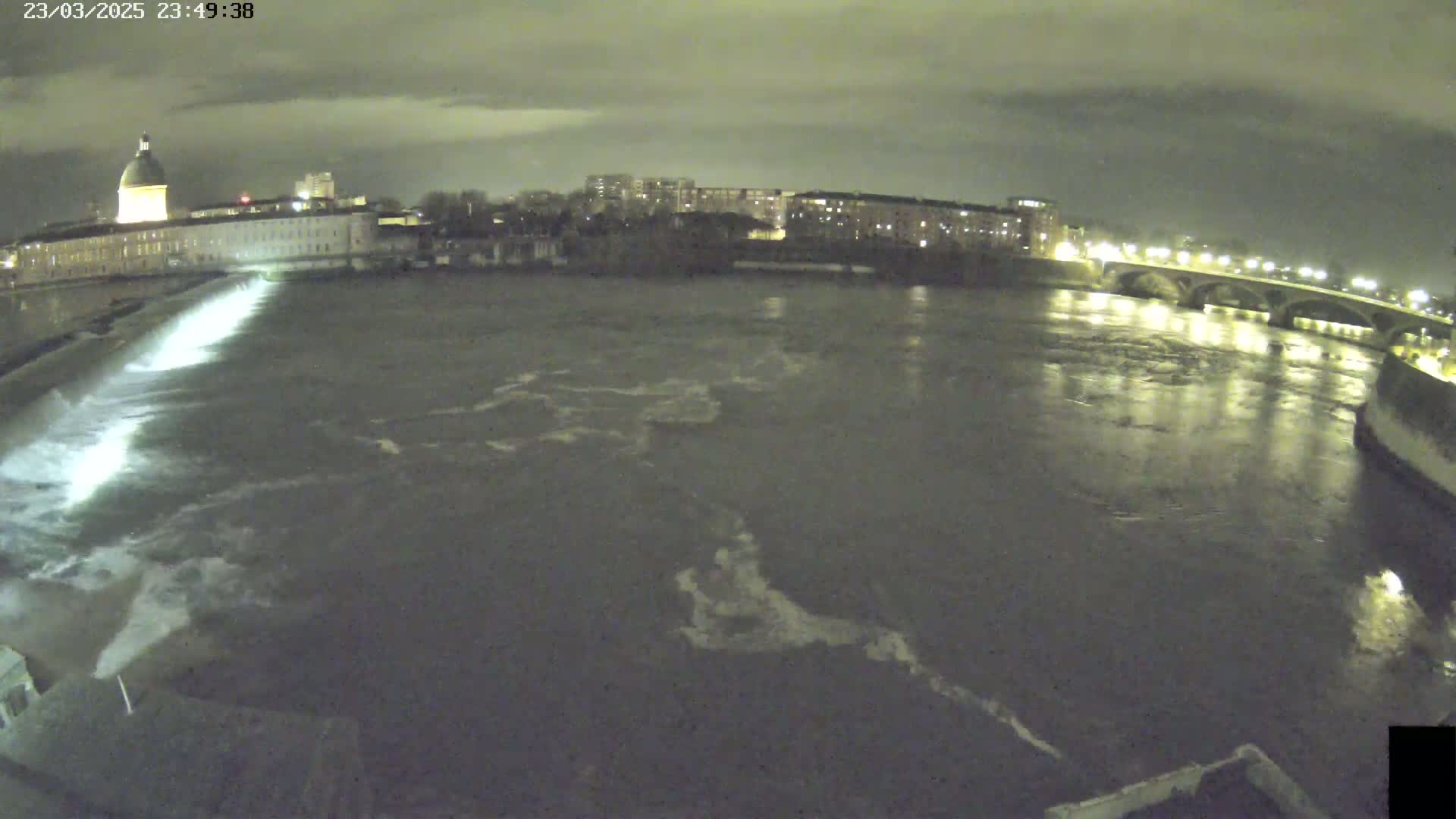 A nighttime view of a river flowing past a city with a building featuring a dome, under a cloudy sky.