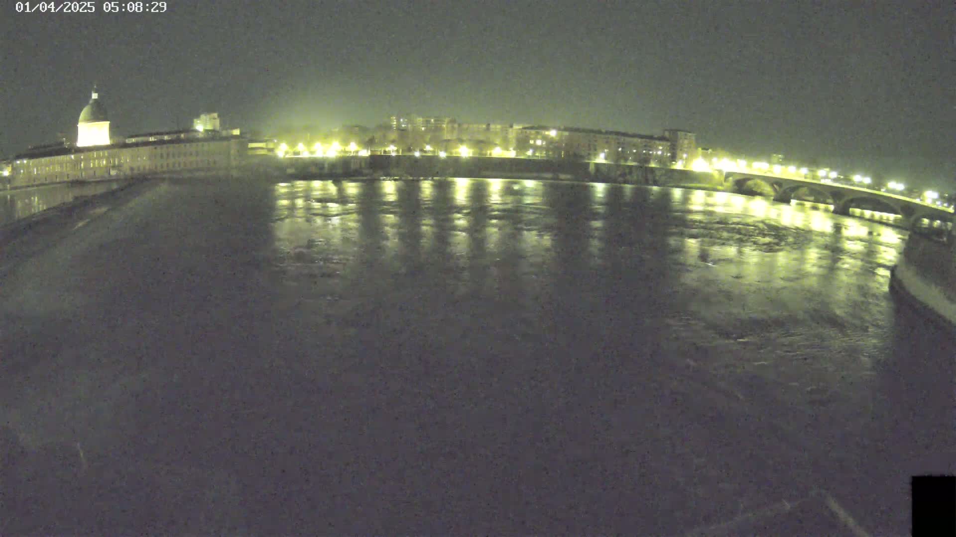 A nighttime view of a calm river reflecting the lights of a city's buildings and a bridge.