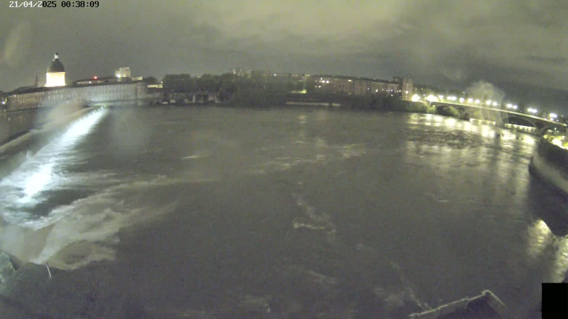 A nighttime view of a river flowing past a city with a building featuring a dome, under a cloudy sky.