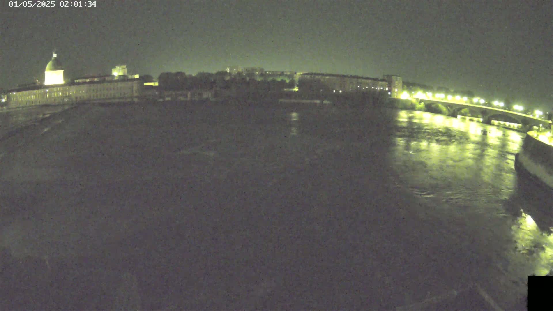 A nighttime view of a river flowing under a bridge, with buildings and lights visible on both banks.