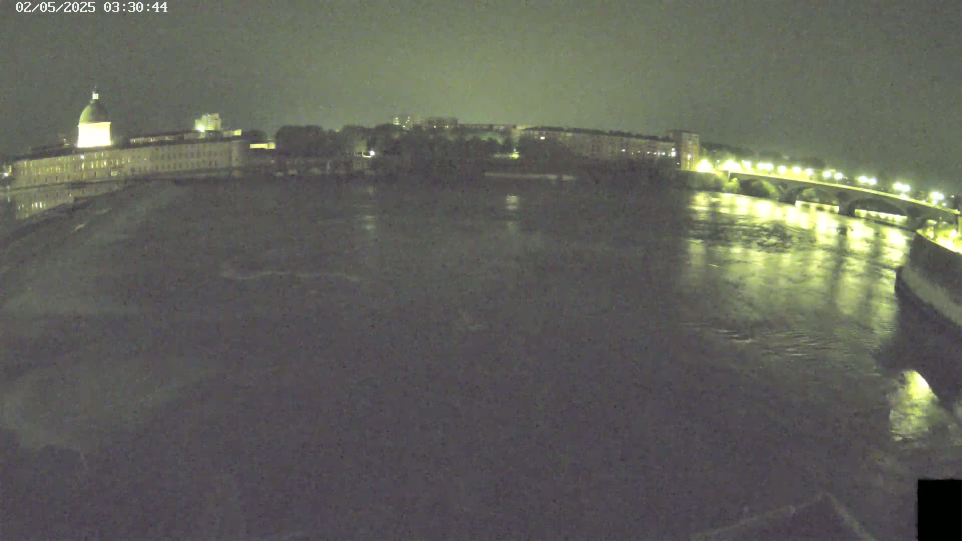 A nighttime view of a river flowing past a city with a large building and a lit bridge.
