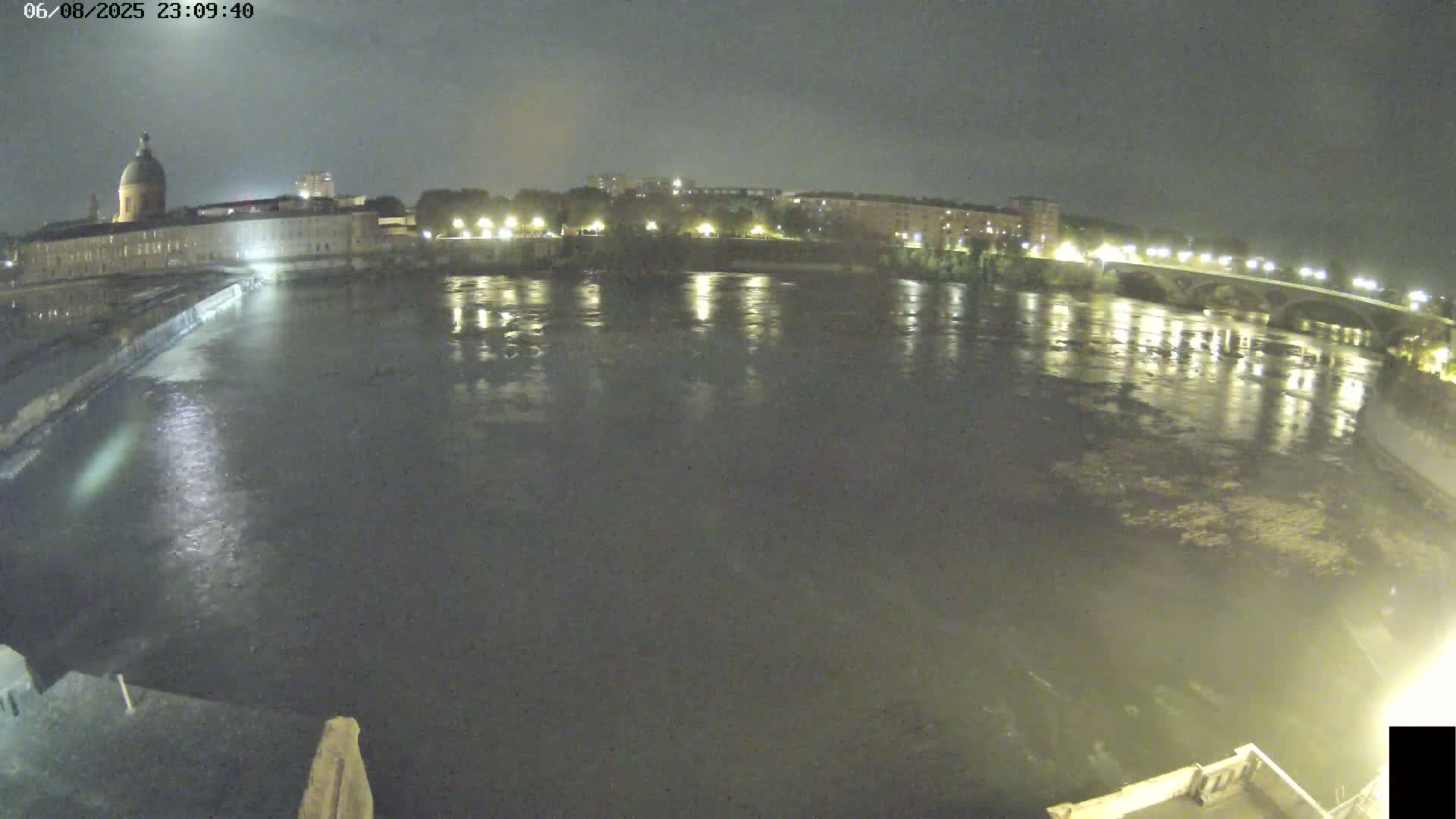 A nighttime view shows a river reflecting city lights, a large domed building on one bank, and a bridge spanning the river in the distance.