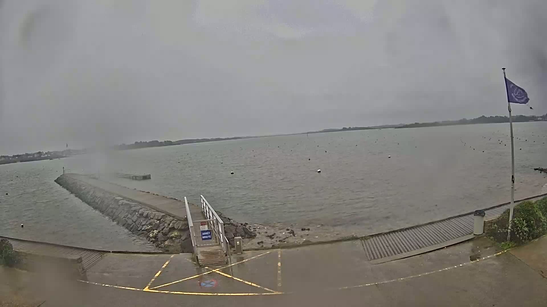 A stone jetty extends into a calm, grey body of water under an overcast sky.