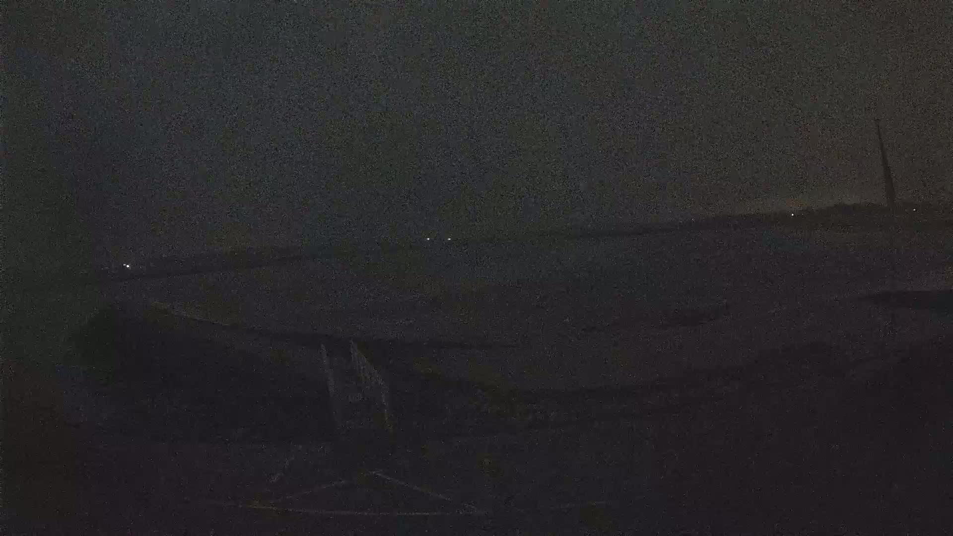 A dark, nighttime scene shows a body of water with faint lights in the distance and a shadowy, indistinct foreground.
