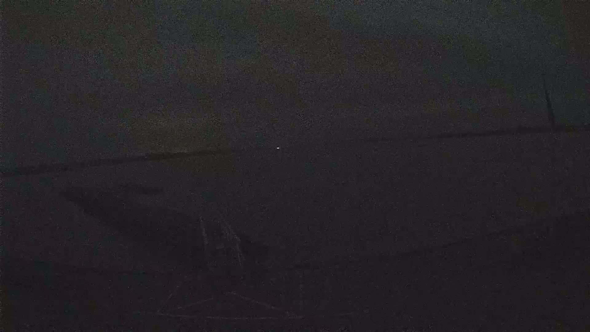 A dark, blurry nighttime image shows a flat, dark expanse of land or water with a single faint light in the distance.