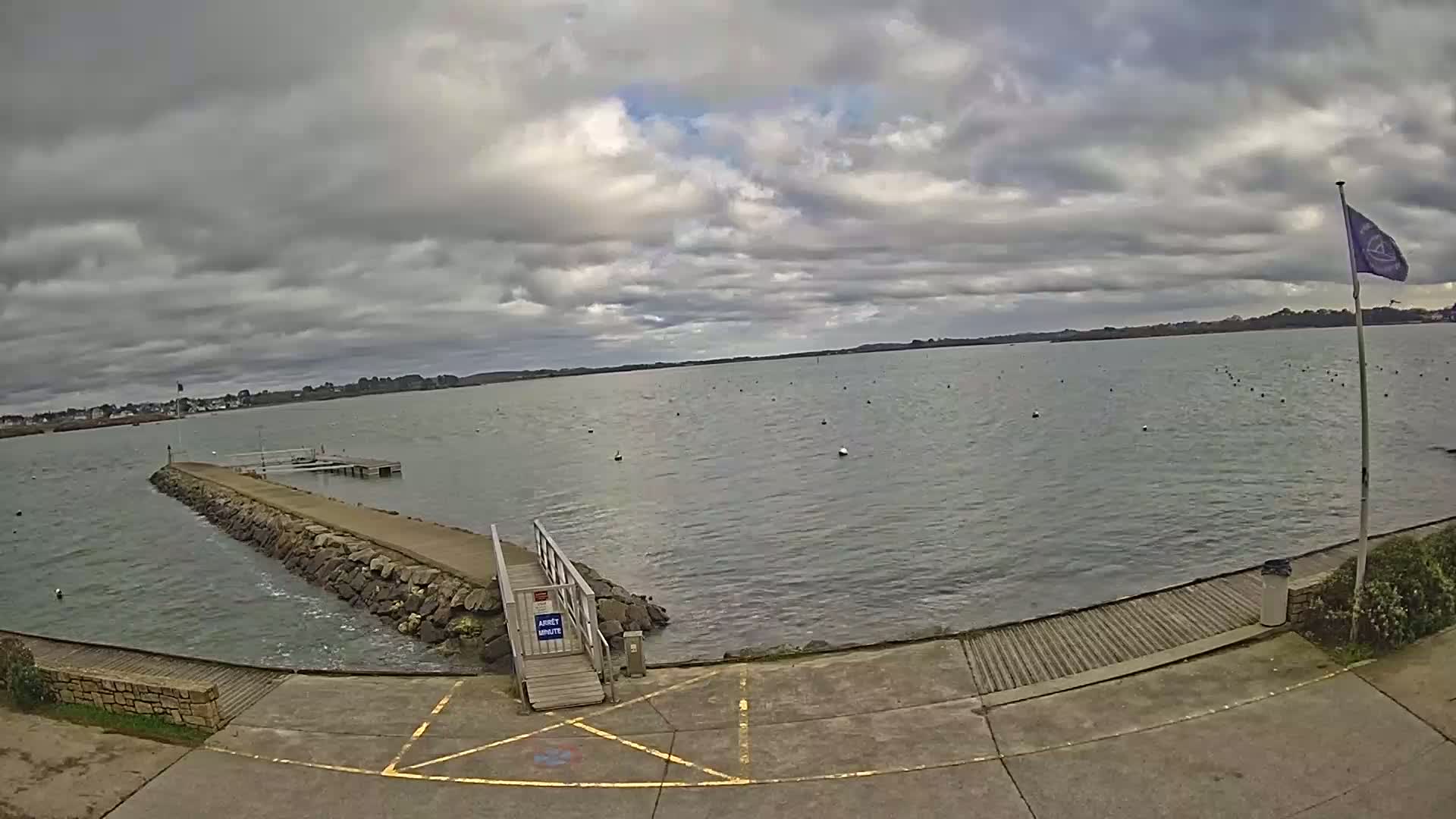 A rocky jetty extends into a calm body of water under a cloudy sky.