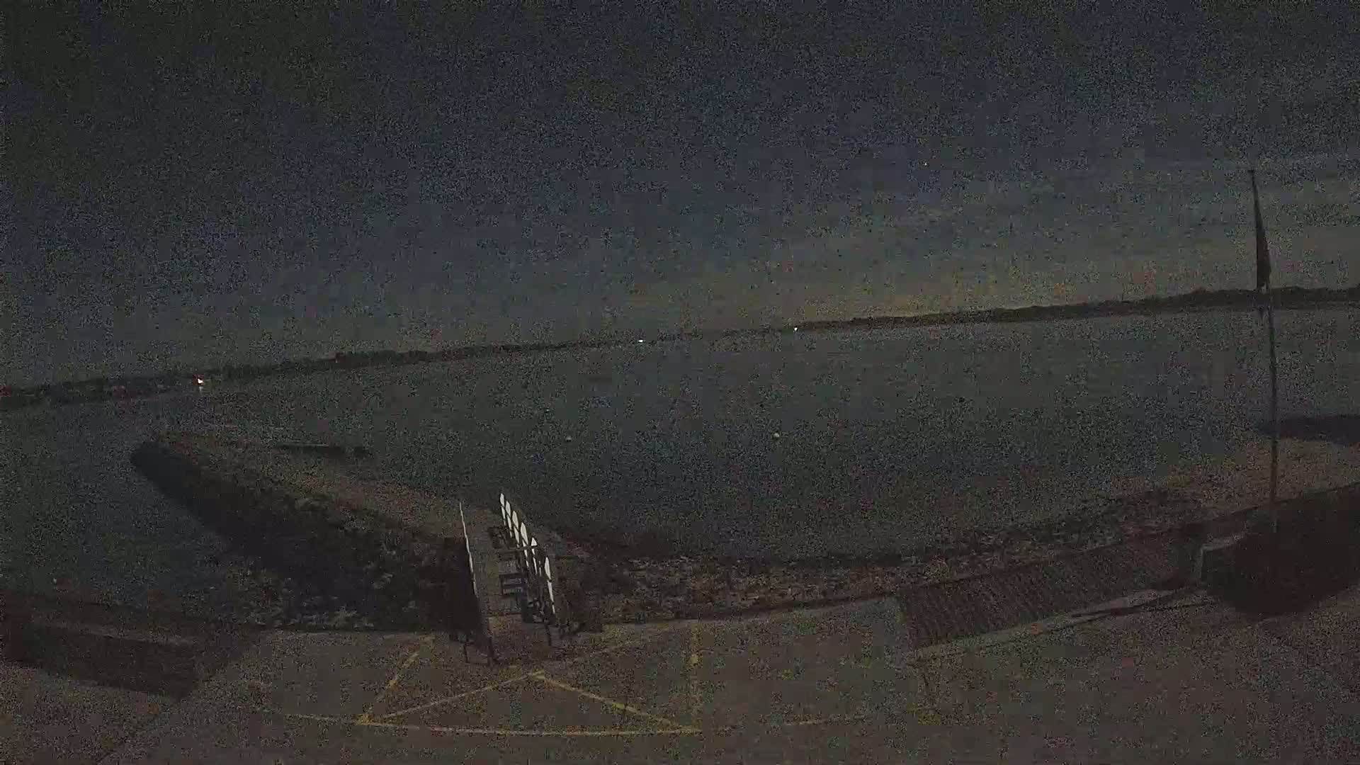 A dark, nighttime view of a calm body of water with a small pier and a flagpole visible in the foreground.