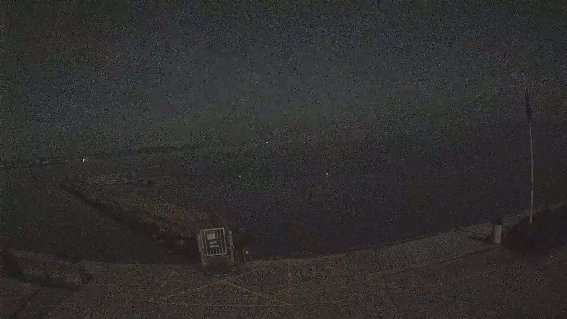 A dark nighttime view of a calm body of water with a dock and a gate in the foreground under a cloudy sky.