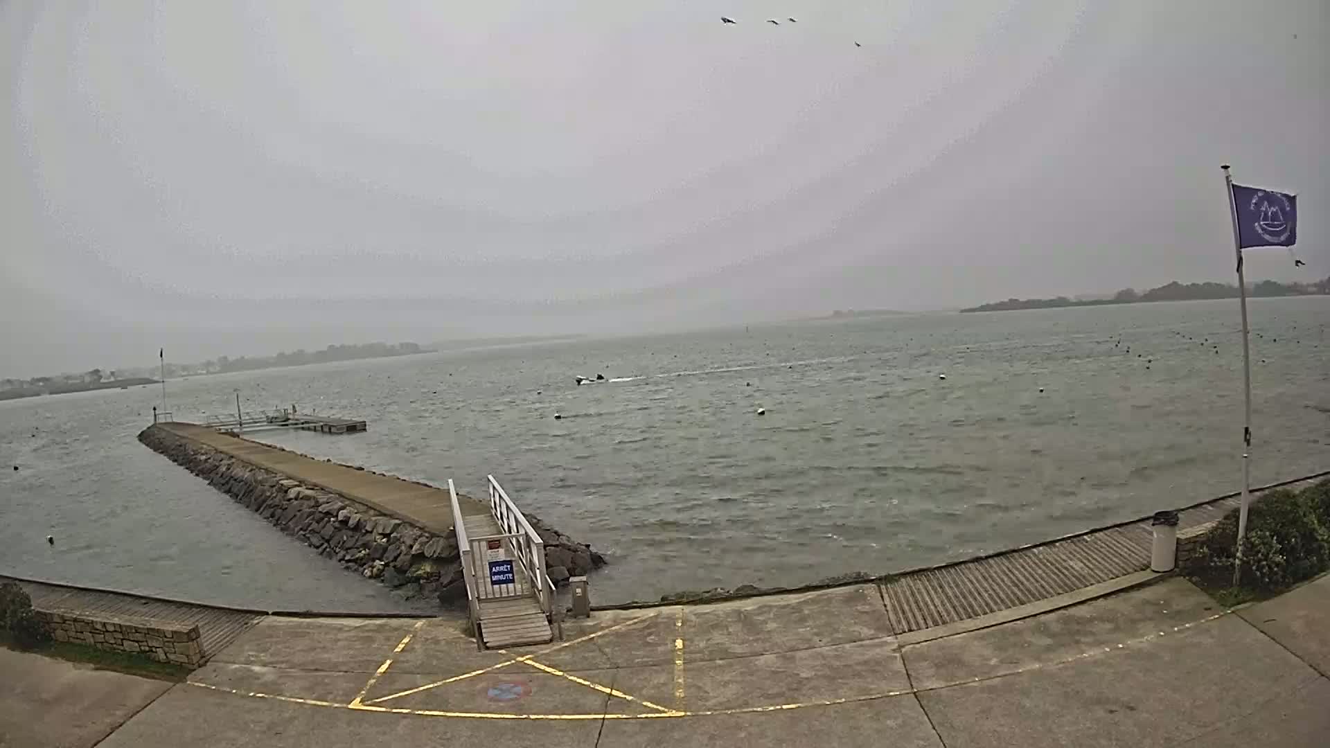 A long, stone jetty extends into a choppy, gray body of water under an overcast sky.