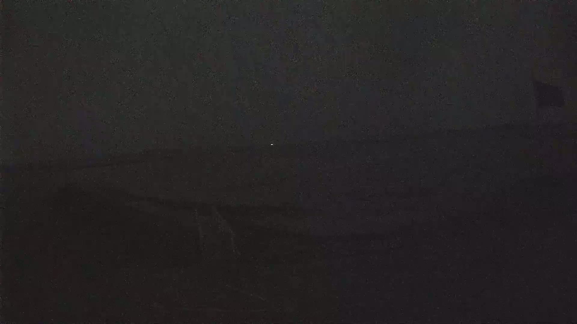 A dark, nighttime scene shows a small, distant light source in a mostly obscured landscape.